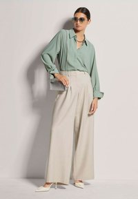 Grüne Langarmbluse, hoch taillierte beigen weite Hosen, silberne Clutch und cremefarbene spitze High Heels, ergänzt durch übergroße Sonnenbrillen.