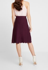 Jupe côtelée bordeaux avec un ourlet en forme de coquille, associée à un top à bretelles spaghetti rose. Le mannequin porte des bottines beiges.