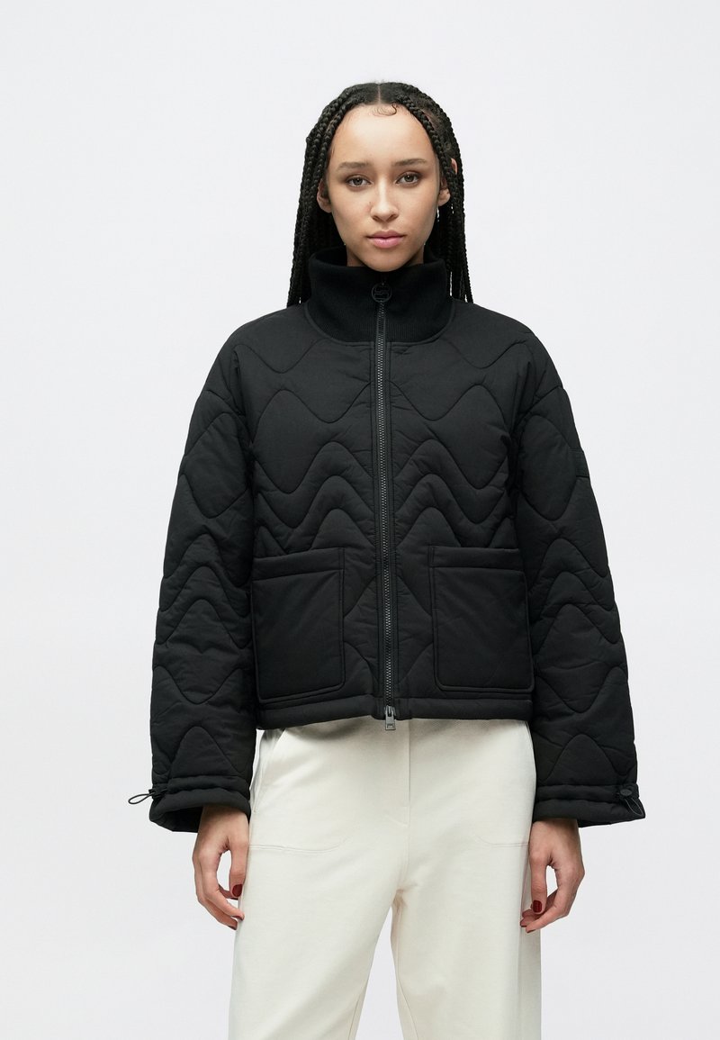 Czarna pikowana kurtka z wysokim kołnierzem, przednim zamkiem błyskawicznym i dwoma dużymi naszywanymi kieszeniami; posiada teksturowany wzór fali oraz elastyczne mankiety.