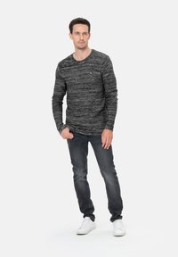 Camisa de punto negra y gris jaspeado de manga larga con cuello redondo, combinada con jeans oscuros y zapatillas blancas. Logo pequeño en el pecho.