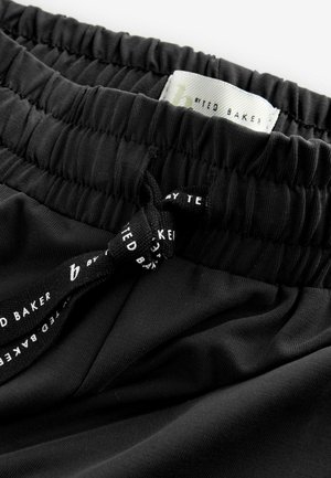 Des joggers noirs avec taille élastique présentent un cordon de serrage avec un texte de marque, une texture lisse et un tissu légèrement froncé à la taille.