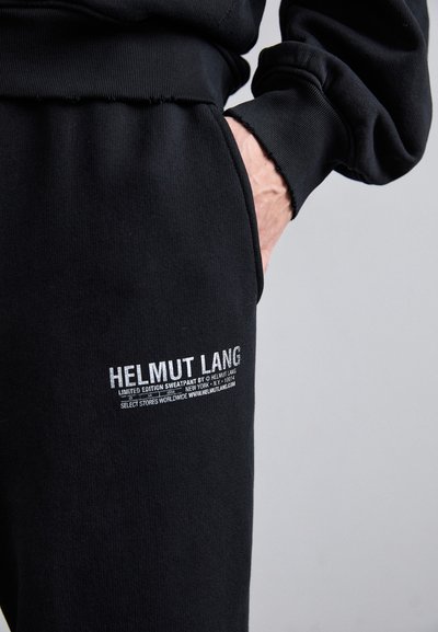 Czarne, limitowane edycje spodni dresowych marki Helmut Lang, z żebrowanym pasem, miękką fakturą i białymi nadrukami logo na nogawce.