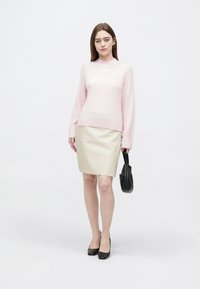 Svetloružový pletený sveter s dlhými rukávmi, doplnený béžovou koženou sukňou ceruzkového strihu. Čierna kabelka a topánky dotvárajú outfit.