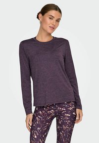 Lilla langærmet top med rund hals, lavet af blød, struktureret stof; parret med mønstrede leggings i nuancer af mørkelilla og orange.