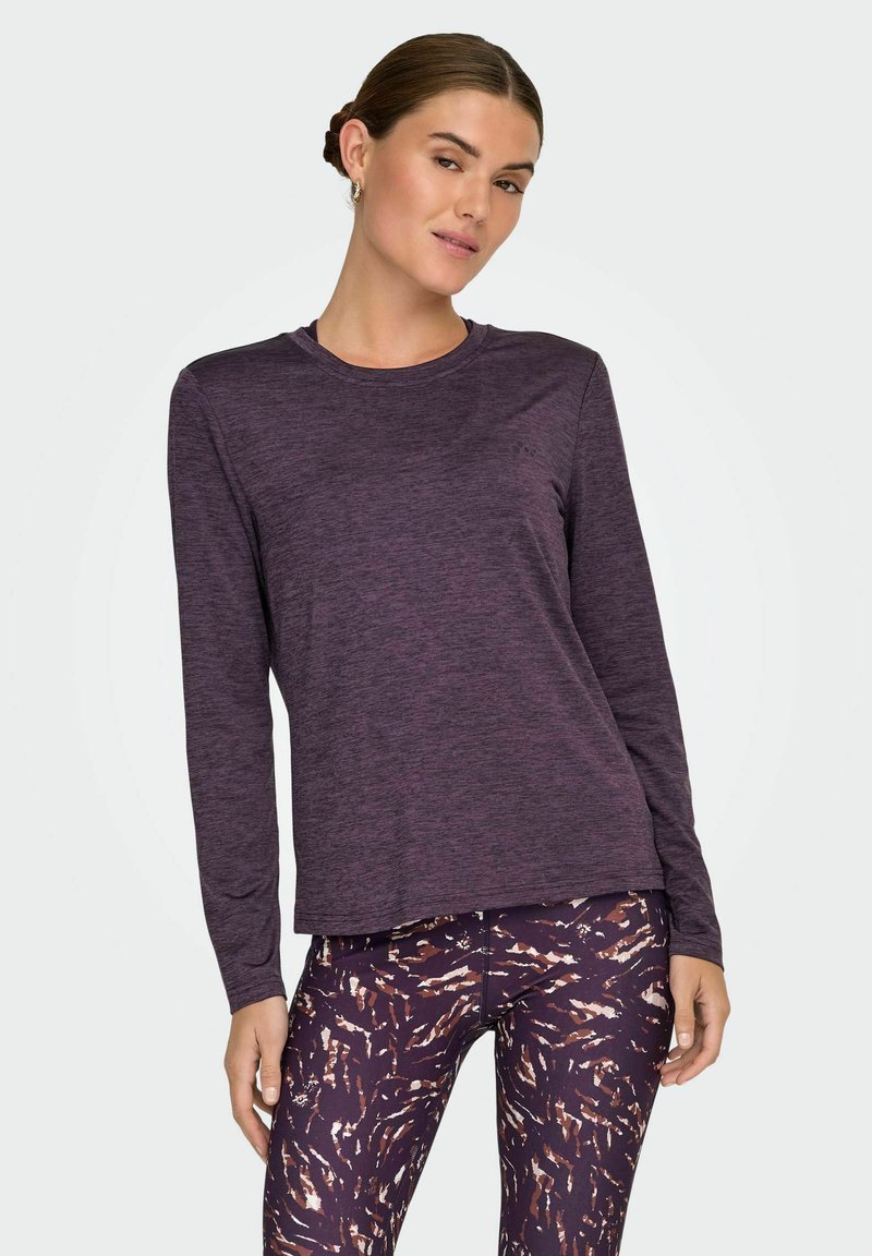 Lilla langærmet top med rund hals, lavet af blød, struktureret stof; parret med mønstrede leggings i nuancer af mørkelilla og orange.