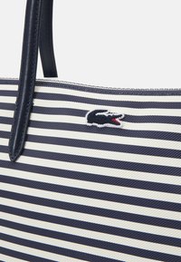 Sac fourre-tout rayé en tissu bleu marine et blanc, avec une finition texturée et un détail en logo brodé. Poignées durables pour le transport.