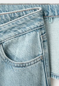 Svetlomodré riflové džínsy so zameraním na predné vrecko a pás s viditeľným prešívaním a vyblednutou textúrou látky.