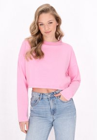Sudadera corta rosa con mangas largas, cuello redondo y textura suave, combinada con unos jeans de mezclilla azul claro de cintura alta.