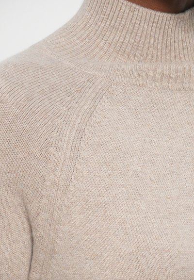 Beżowy sweter z golfem z miękkiej dzianiny, z prążkowanym kołnierzem i szwami na ramionach oraz delikatnym teksturowanym wykończeniem krawędzi.