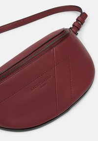 Borsa a tracolla in pelle bordeaux con forma curvata, chiusura superiore a zip e logo in rilievo. Presenta una texture liscia e dettagli di cucitura minimalisti.