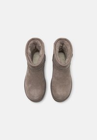 Paire de bottes d'hiver beiges en suède avec doublure intérieure douce et duveteuse, vues de dessus sur un fond clair uni.