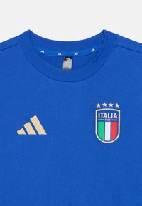 Μπλε βαμβακερό t-shirt με στρογγυλή λαιμόκοψη, χρυσό λογότυπο Adidas και κεντητό έμβλημα της εθνικής ομάδας ποδοσφαίρου της Ιταλίας με τέσσερα αστέρια από πάνω.
