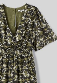 Robe à manches courtes avec un motif abstrait vert et noir. Présente un décolleté en V profond, des détails de boutons et une taille smockée. Tissu léger.