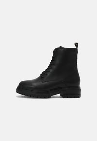 Bottines en cuir noir avec un design à lacets, un bout rond et une semelle robuste. Dotées d'une languette à l'arrière pour un enfilage facile.
