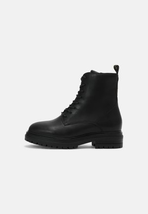 Bottines en cuir noir avec un design à lacets, un bout rond et une semelle robuste. Dotées d'une languette à l'arrière pour un enfilage facile.