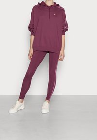 Mörkröd huvtröja med dragsko och ribbade ärmslut, parat med matchande leggings med sidostråk. Kompletteras med ljusa sneakers.