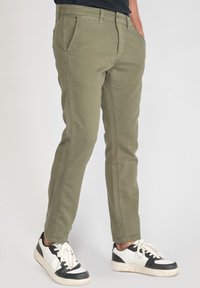 Chinos vert olive avec une coupe slim, dotés de poches avant et d'une texture en coton lisse. Associés à des baskets noires et blanches.
