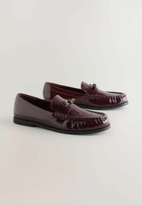 Burgunderfarbene Lackleder Slipper mit abgerundeter Zehe, dekorativem Riemen und subtilen Nähdetails. Schwarze Gummisohle.