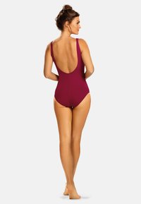 Bordowy jednoczęściowy strój kąpielowy z niskim plecami, cienkimi ramiączkami i gładkim, dopasowanym materiałem. Brak widocznych wzorów lub elementów metalowych.