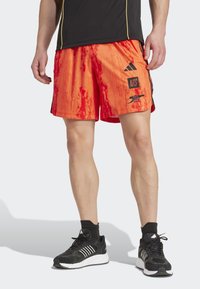 Orange og røde sportsshort med et gradientm�ønster, prydet med sorte accenter og branding. Parret med sorte sneakers og sokker.