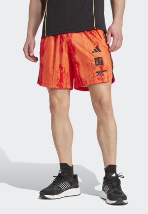 Oranje en rode sportshorts met een gradientpatroon, voorzien van zwarte accenten en branding. Gecombineerd met zwarte sneakers en sokken.