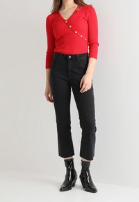 Czerwony prążkowany sweter z dzianiny z rękawami do łokcia i ukośnym rzędem guzików, zestawiony z czarnymi, wysokim stanem jeansami i błyszczącymi czarnymi botkami za kostkę.