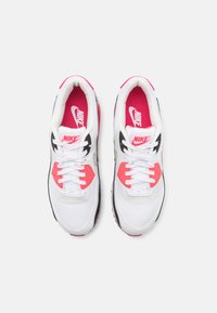 Ténis Nike com um upper de malha branca, detalhes em rosa, pormenores em preto e atacadores brancos. Sola de borracha texturizada para tração.