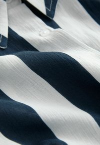 Camicia a righe con strisce orizzontali blu navy e bianche, realizzata in un tessuto leggero con una morbida texture e dettagli con colletto a bottoni.