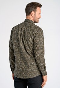 Camisa de manga larga de estampado floral marrón con cuello abotonado y dobladillo recto, que presenta pequeñas flores azules, blancas y amarillas.