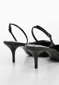 Sandales noires à talons hauts avec une finition brillante, à bout ouvert et des brides fines à la cheville. Les talons sont effilés et au design élégant.
