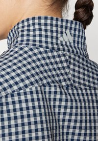 Μπλε και λευκό καρό πουκάμισο με ανρθρωπό λαιμό, ενισχυμένο γυαλό και μια διακριτική λογότυπο λεπτομέρεια στον πίσω λαιμό.