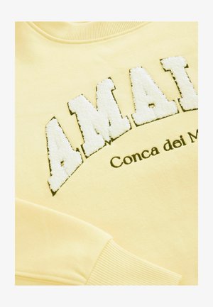 Kollane dressipluus, millel on valge tekstureeritud tikandiga "AMAI" musta äärisega. Allpool on mustas trükis "Conca dei Marmi". Ribaga krae ja varrukad.