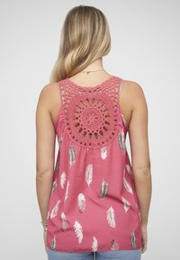 Roze mouwloos topje met een haakwerk aan de achterkant. Heeft een veerpatroon in wit en grijs. De stof lijkt lichtgewicht en textuurrijk.