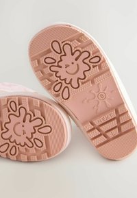 Roze rubberen schoenzool met een glimlach design, gestructureerde grip en een doorzichtige sectie met maatindicatie aan de zijkant.