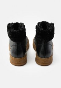 Botas negras hasta el tobillo con un suave cuello de piel sintética negra, parte superior de cuero y suela de goma. Presentan un cremallera lateral para facilitar el uso.