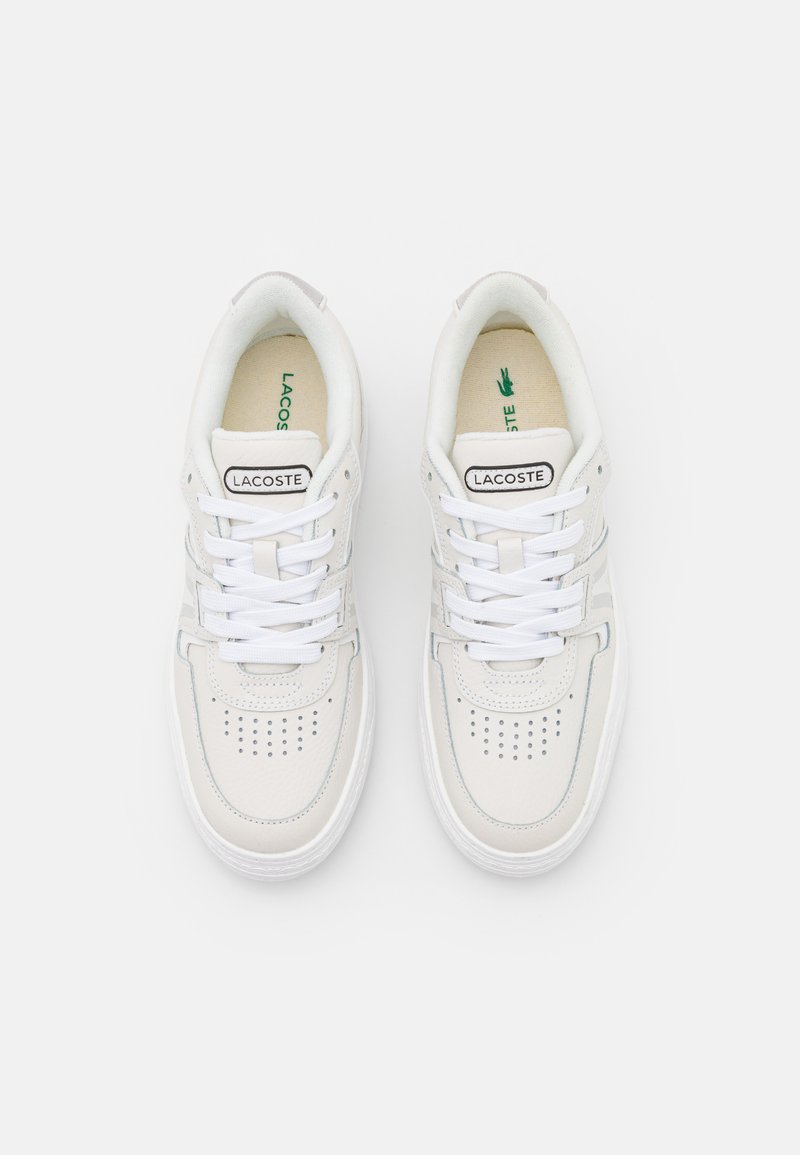 Baskets Lacoste blanches avec des détails perforés, un design structuré, des lacets plats et une texture de cuir douce et lisse. Logo vert sur la semelle intérieure.