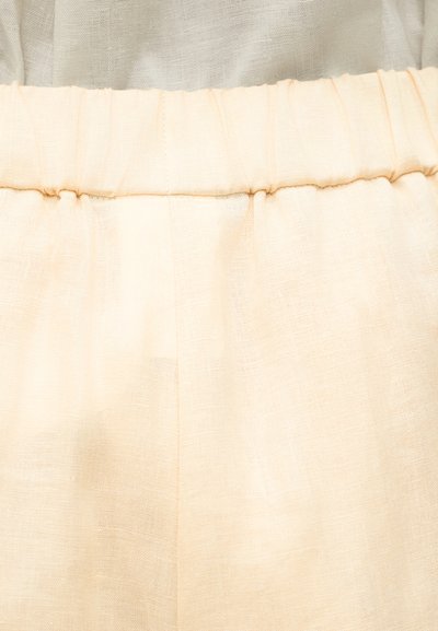 Prim-plan cu material de in bej cu o talie elastică pe un articol vestimentar, evidențiind textura și pliurile moi.