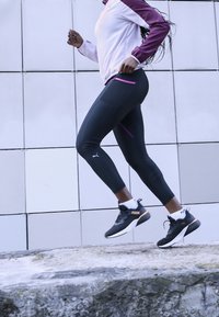 Leggings de sport noirs avec des accents violets et une coupe ajustée, associés à une veste zippée blanche et bordeaux ainsi qu'à des chaussures de course noires.