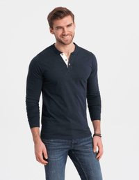 Leende man i en marinblå långärmad henley-tröja med tre knappar och blå jeans, stående mot en vit bakgrund.