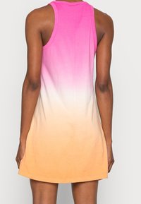 Donna che indossa un vestito senza maniche con un gradiente di rosa, bianco e arancione, vista da dietro su uno sfondo chiaro e semplice.