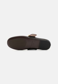 Scarpa nera con una tomaia in pelle liscia, un accento taupe a contrasto e un tacco basso. La suola è in gomma con una superficie piana e testurizzata.
