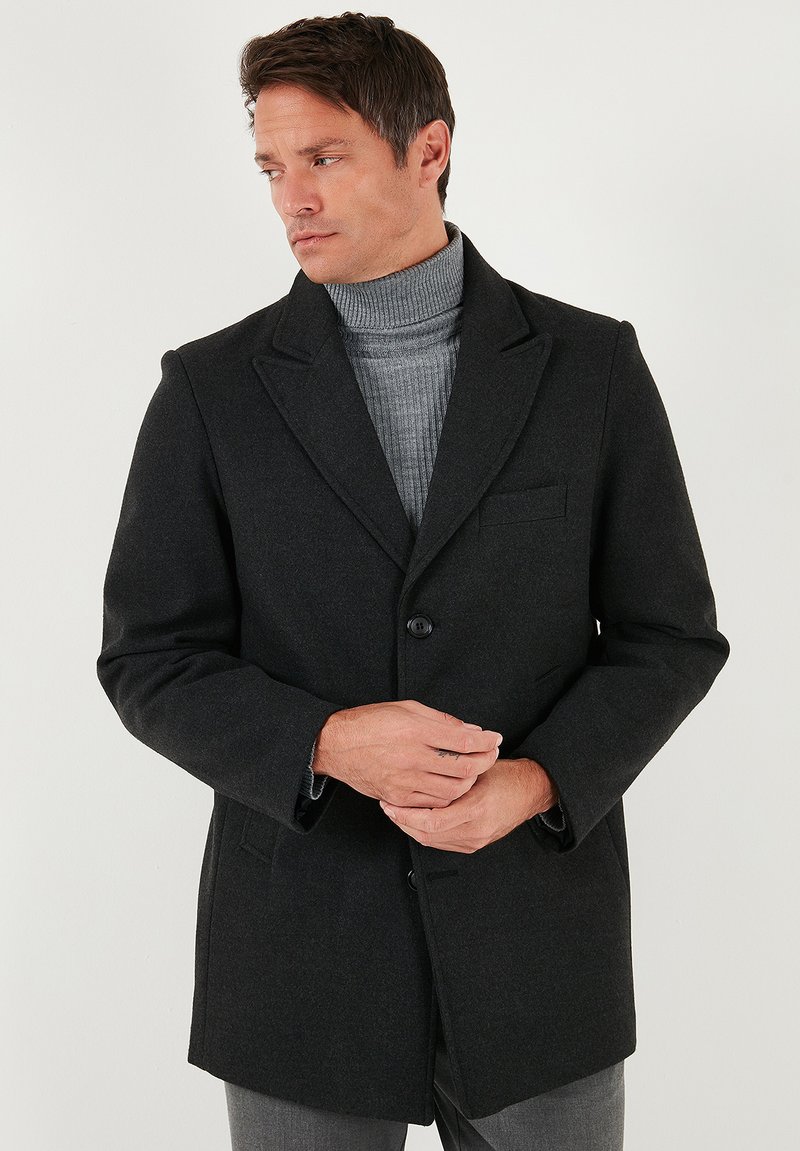 Mustast villasegust mantel ühe nupuga, mitteeritud kraede ja rinnataskuga. Sellel on pehme tekstuur ja istuv lõige.