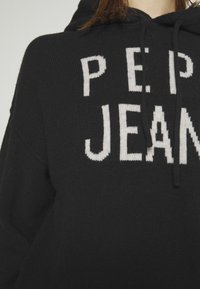 Sweat à capuche noir avec "PEPE JEANS" tricoté en blanc. Il présente une texture douce, des cordons de serrage réglables et une coupe décontractée.