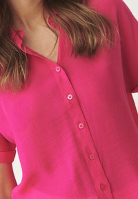 Camicia rosa a maniche corte con bottoni in tessuto testurizzato, caratterizzata da bottoni abbinati e scollatura a V.