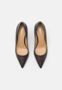 Escarpins en cuir marron à talons hauts avec une pointe fine et des côtés découpés, présentant une texture lisse et une semelle intérieure beige clair avec un logo.