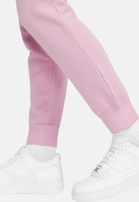 Ljusrosa svettbyxor med ribbade muddarna som är kombinerade med vita sneakers, med en slät textur och subtila sidsömmar.
