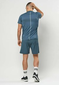 Camiseta deportiva de manga corta azul con un patrón vertical central, combinada con pantalones cortos a juego. Se lleva con calcetines blancos hasta la mitad de la pantorrilla y zapatillas negras.