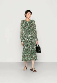Vestido com estampa floral em verde, branco e preto; mangas bufantes longas; corpete plissado; comprimento midi; combinado com uma bolsa preta e sandálias rasas.