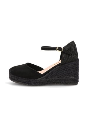 Zapato de esparto con cuña negra, correa en el tobillo y hebilla, punta cerrada y suela de plataforma trenzada.