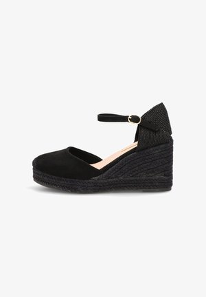 Zapato de esparto con cuña negra, correa en el tobillo y hebilla, punta cerrada y suela de plataforma trenzada.